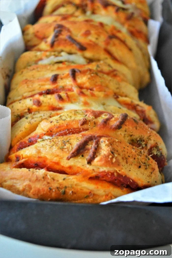 Pizza Monkey Bread 8 A close-up of a single slice of pull apart pizza bread, highlighting the texture of the biscuit dough and the generous pepperoni and cheese filling.