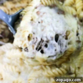 Close-up of creamy, cheesy rotini pasta with ground meat, reminiscent of a savory instant pot cheesesteak dish, being scooped with a serving spoon.