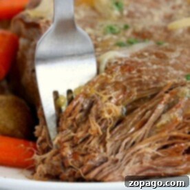 Close-up of a fork shredding tender pot roast made in a Ninja Foodi, with carrots and potatoes in the background.