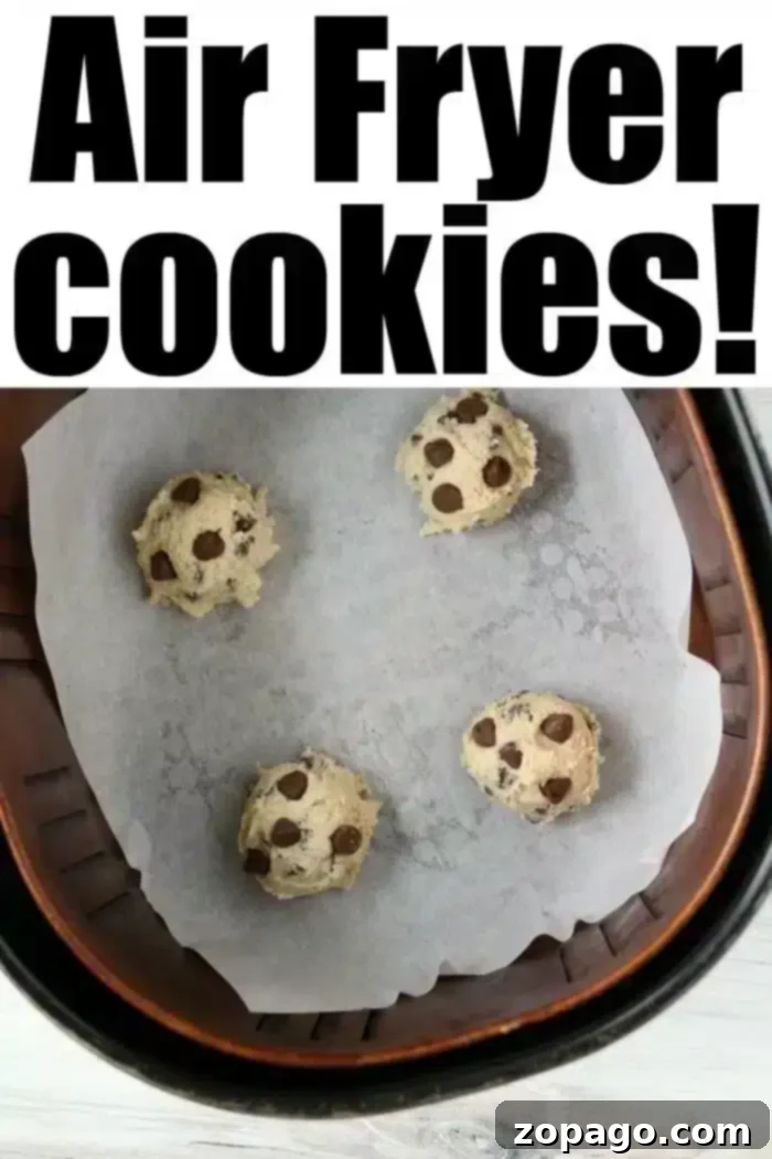 Perfect Air Fryer Chocolate Chip Cookies 5 Four balls of chocolate chip cookie dough sit on parchment paper in an air fryer basket. The words “Delicious Air Fryer Cookies!” proudly top the image, promising a sweet treat.