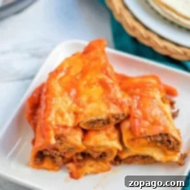A plate of cheesy beef enchiladas, made perfectly in an instant pot, is artfully stacked on a white square plate with a hint of tortillas in the background.