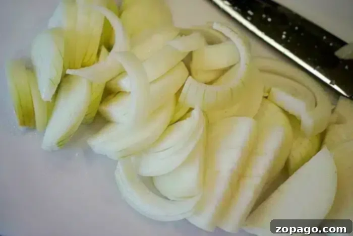 Golden Crisp Air Fryer Onions 5 Slices of white onion on a cutting board next to a knife, ready to be transformed into crispy air fryer onions.
