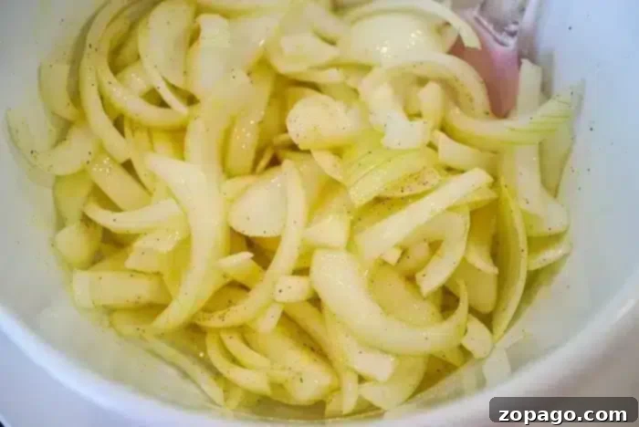 Golden Crisp Air Fryer Onions 7 A close-up image of sliced onions in a white bowl, seasoned with a light sprinkling of salt and pepper after being perfectly crisped in the air fryer.