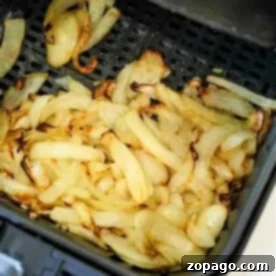 Sliced onions are being expertly cooked and slightly browned in the air fryer basket, transforming into deliciously crispy air fryer onions.