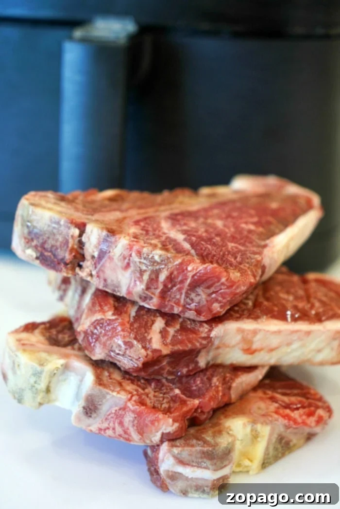 Easy Air Fryer Steak Bites 3 A pile of raw steaks, perfect for transforming into tender air fryer steak bites, is stacked on a counter against a dark background, ready for cooking bliss.