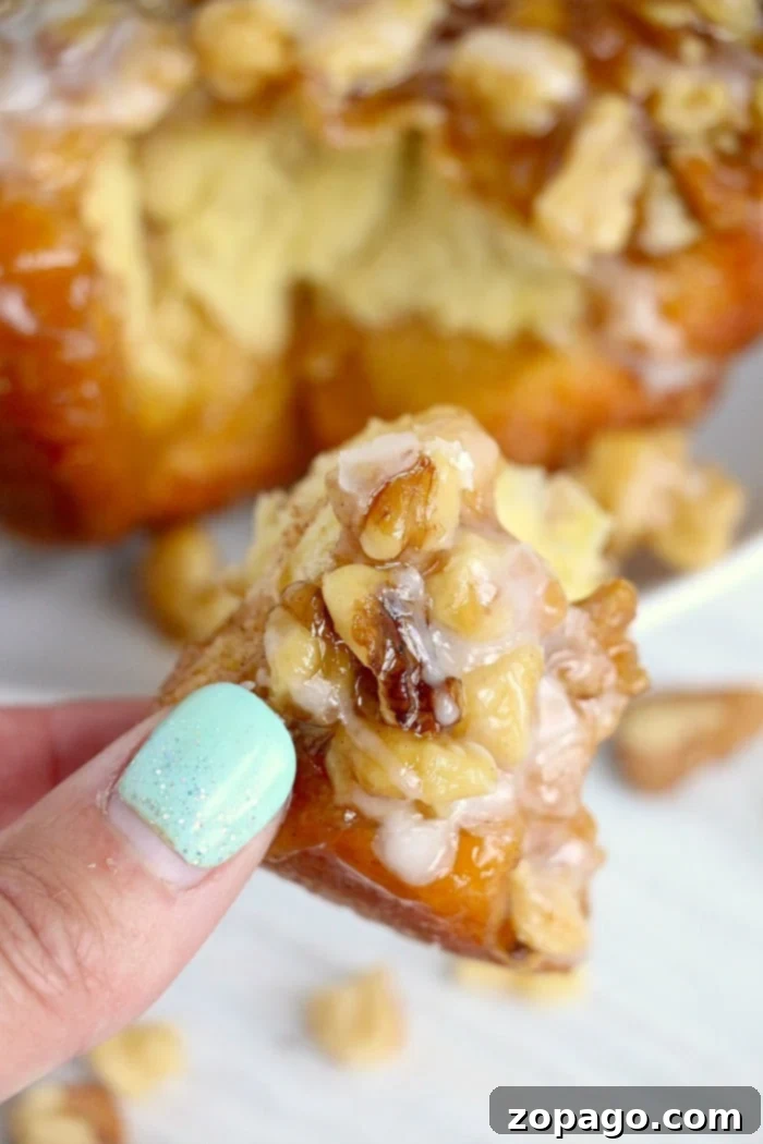 Easy Air Fryer Monkey Bread 2 A hand with mint green nails holds a piece of glazed air fryer monkey bread creation, showcasing its sticky, pull-apart texture.