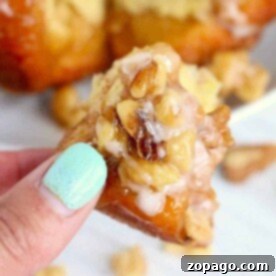 Close-up of a hand holding a piece of sticky nut pastry, reminiscent of air fryer monkey bread, with walnuts and icing.