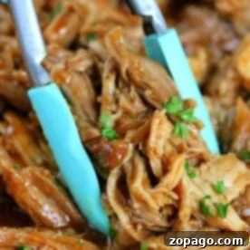 Close-up of a pair of tongs holding Ninja Foodi pulled pork, garnished with chopped herbs.