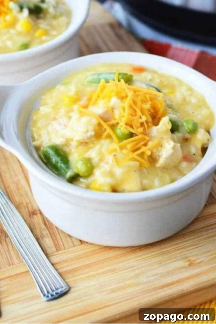 One-Pot Chicken Casserole 2 A bowl of creamy chicken and rice topped with shredded cheese on a wooden board, reminiscent of a comforting crockpot chicken casserole, sits invitingly beside a fork.