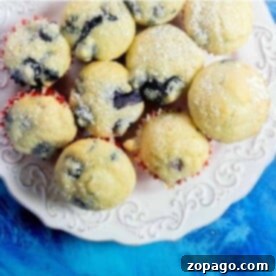 Pancake Mix Muffin Hack 7 A plate of blueberry pancake mix muffins dusted with powdered sugar on a blue background.