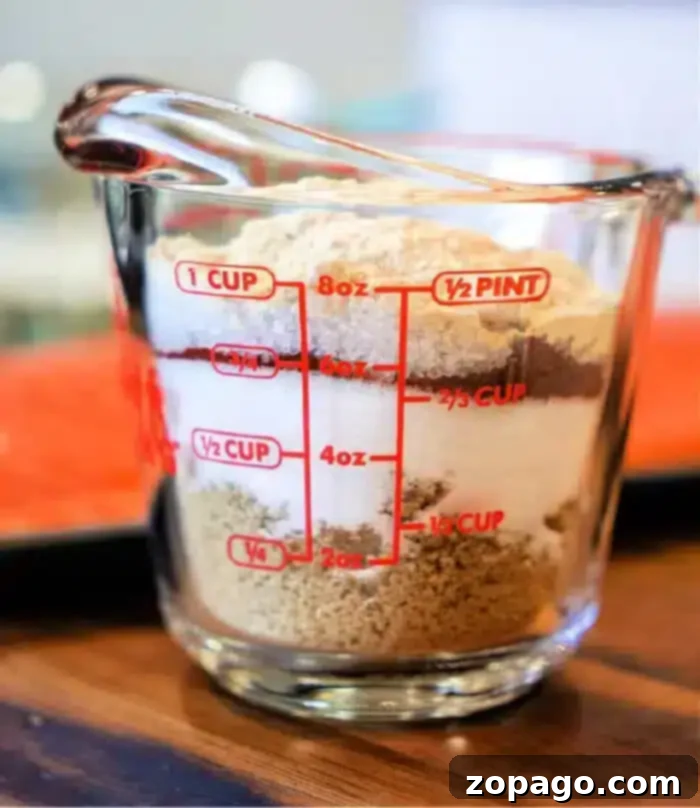 Ultimate Salmon Spice Blend 2 A clear measuring cup filled with layered ingredients, including brown sugar, flour, and a touch of salmon dry rub. The cup features red measurement markings for cups, ounces, and pints. It rests on a wooden surface.