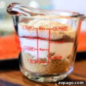 Ultimate Salmon Spice Blend 8 A clear measuring cup filled with salt and brown sugar sits on a wooden surface, resembling the perfect blend for a salmon dry rub.