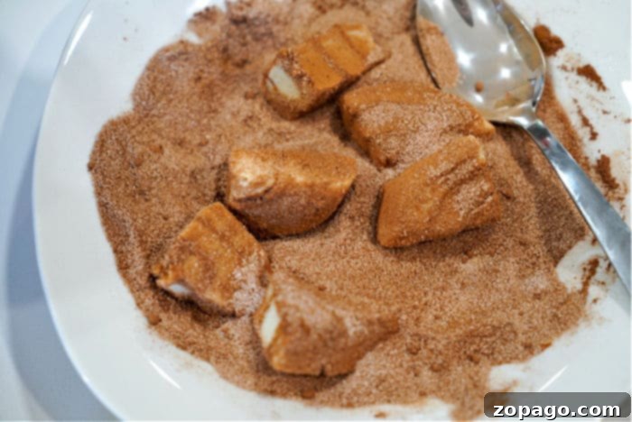 Ooey-Gooey Rhodes Rolls Monkey Bread 5 Cinnamon roll slices coated in cinnamon sugar on a white plate with a spoon, reminiscent of the comforting allure of Rhodes monkey bread.