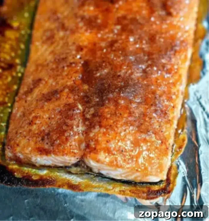Ultimate Baked Salmon 2 Close-up of a perfectly baked salmon fillet on a foil-covered surface. The salmon boasts a beautiful golden-brown, seasoned crust and glistens, indicating its freshness and recent cooking. Around the edges, some caramelized sauce suggests a deeply flavorful preparation, making for an appetizing presentation.