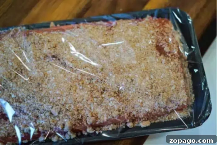 Ultimate Baked Salmon 7 The tray of raw meat, enveloped in a brown breadcrumb seasoning and wrapped in clear plastic, brings to mind the best baked salmon dishes. It rests serenely on a wooden surface, inviting culinary inspiration.