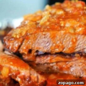 Petite Brisket 7 Close-up of savory brisket, slow-cooked in the oven, topped with a rich, chunky tomato sauce.