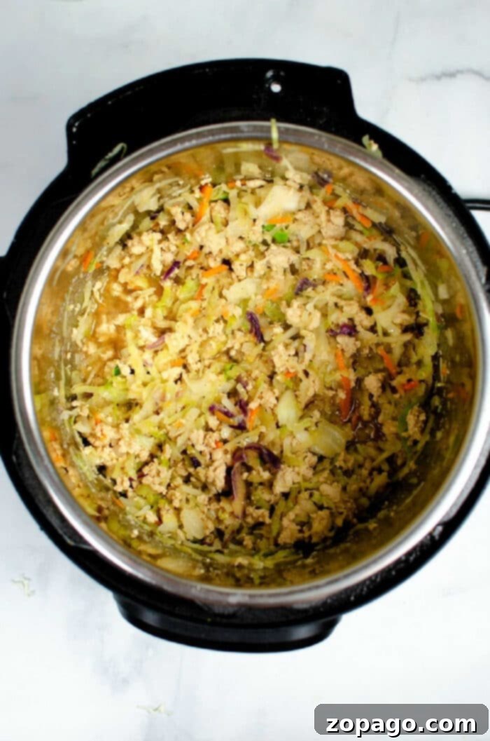 Instant Pot Egg Roll Bowl 4 Shredded vegetables and rice mixture for instant pot Egg Roll in a Bowl inside an Instant Pot on a white surface.