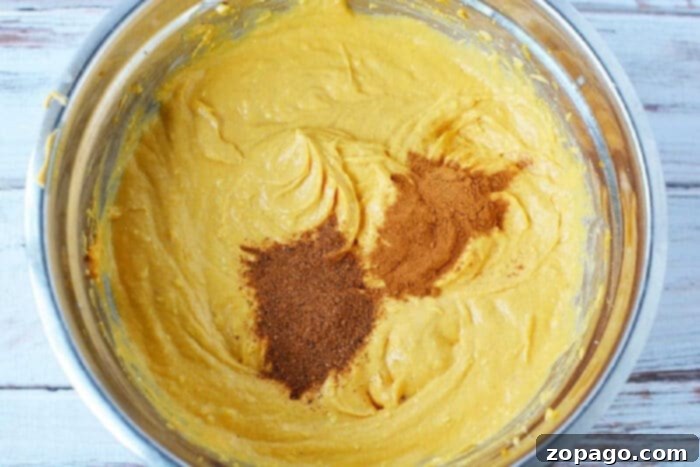Pumpkin Pie Bars 3 Pumpkin batter in a metal bowl with cinnamon and nutmeg sprinkled on top, ready to be baked into a delicious sheet pan pumpkin pie.