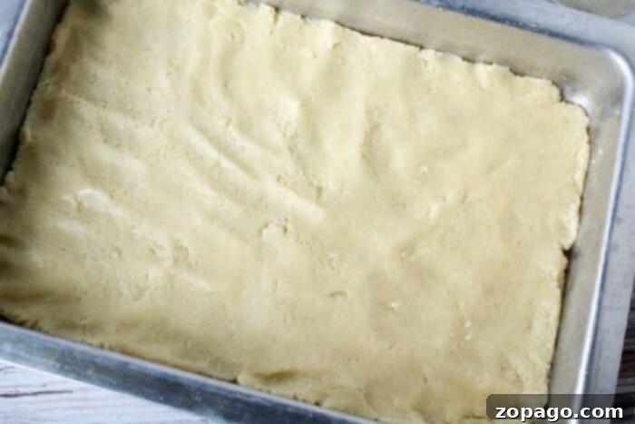 Pumpkin Pie Bars 5 Unbaked sheet pan pumpkin pie dough evenly pressed into a rectangular metal baking pan on a light-colored surface.