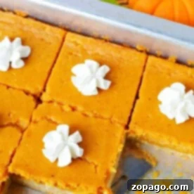 Pumpkin pie sheet cake bars with dollops of whipped cream on a tray, and a small pumpkin in the background.