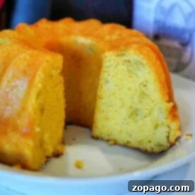 Perfect Air Fryer Cornbread 6 A close-up of a sliced cornbread bundt on a white plate reveals its golden-brown exterior and light, fluffy interior, reminiscent of air fryer cornbread. A bottle with a honey label is partially visible in the background.