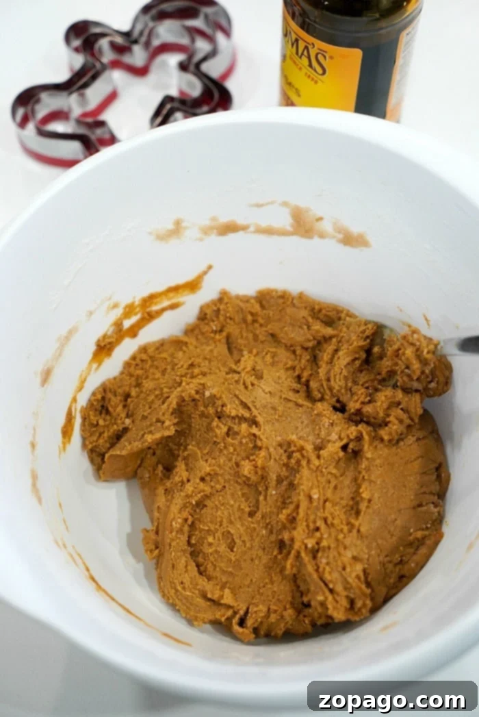 Easy Cake Mix Gingerbread Cookies 5 A white bowl contains rich, unrolled gingerbread dough with a spoon sticking out, hinting at delicious gingerbread cookies to come. A bottle of molasses and various cookie cutters are thoughtfully placed in the background, ready for action.