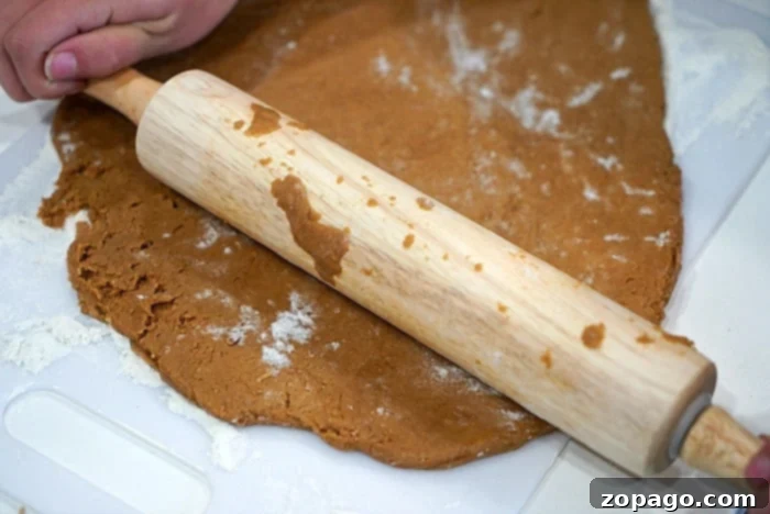 Air Fryer Gingerbread Cookies from Cake Mix 6 Hands rolling out gingerbread cookie dough on a lightly floured surface, preparing for festive cutouts.
