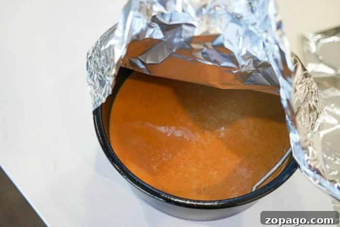 Bite-Sized Pumpkin Pie Delights 8 A bowl of crustless pumpkin pie, is partially covered by aluminum foil on a white surface.