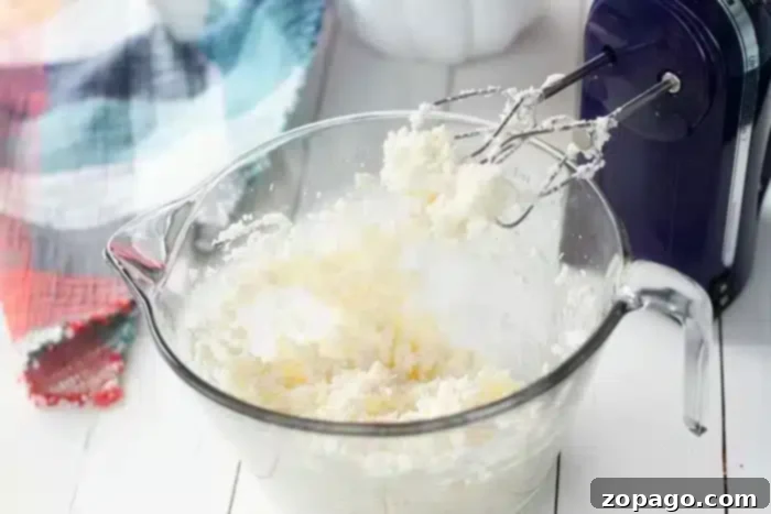Half Sheet Cake Recipe 5 A clear glass mixing bowl filled with creamy frosting, with an electric hand mixer resting in it, ready to whip up frosting for a half sheet cake.