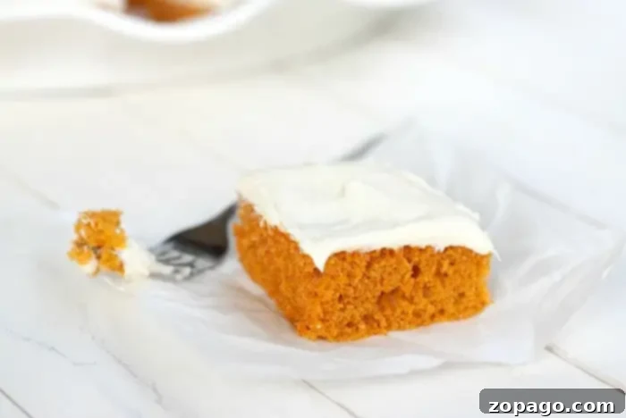 Half Sheet Cake Recipe 6 A perfectly baked and frosted slice of pumpkin cake with white frosting sits on a piece of parchment paper, showcasing its moist texture.