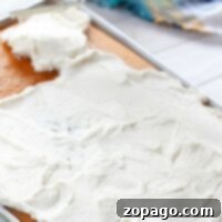 Spreading white frosting smoothly over a 1/2 sheet cake with a spatula.