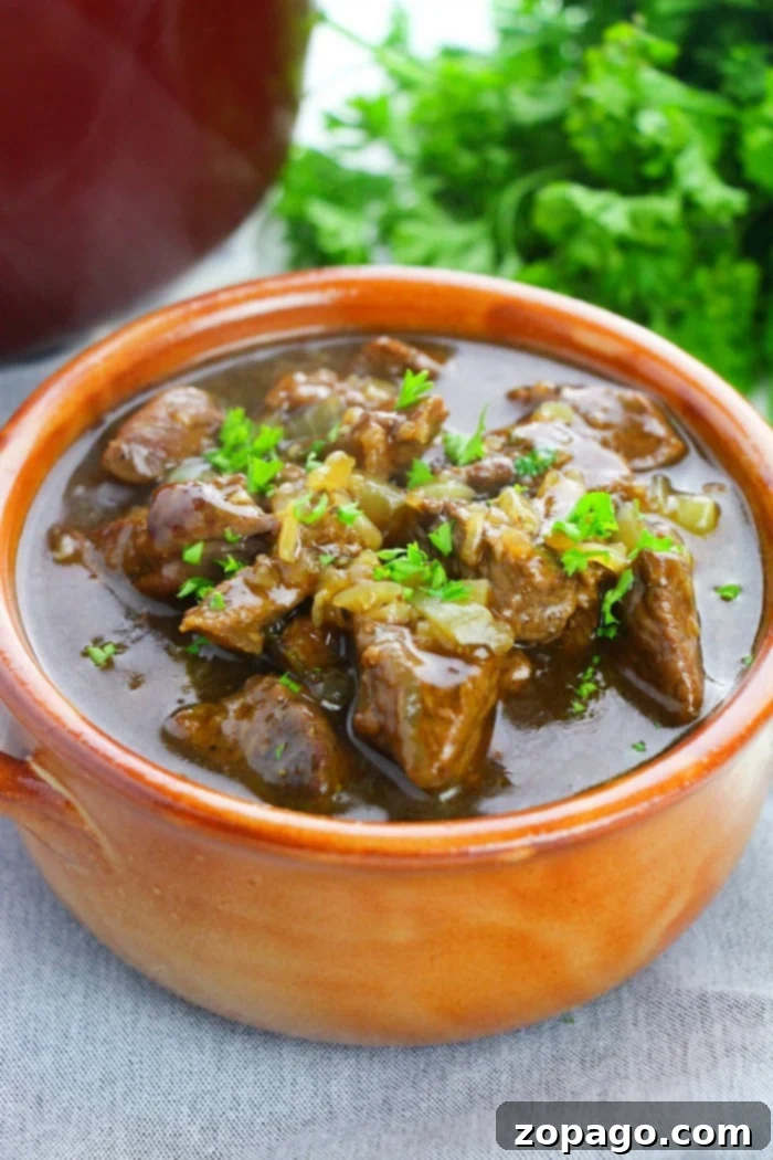 A bowl of beef stew meat garnished with parsley, showcasing perfectly tender beef tips with fresh herbs in the background.