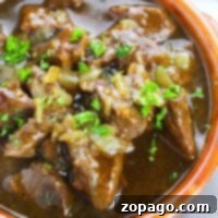 A close-up of a hearty bowl of beef stew garnished with chopped green herbs in a rustic brown ceramic bowl offers a glimpse into how to cook beef tips to perfection.