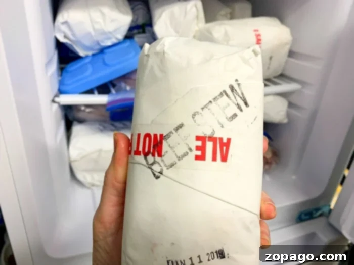 A hand holds a white paper-wrapped package labeled BEEF STEW MEAT, indicating it's ready for an instant pot recipe, with other frozen packages in the background.