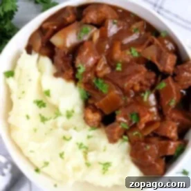 Swift Beef Stew Meat Delights 9 A savory bowl of mashed potatoes topped with beef stew is delicately garnished with parsley, sitting beside a neatly placed fork and napkin. It's a comforting dish that highlights the best in recipes using beef stew meat.