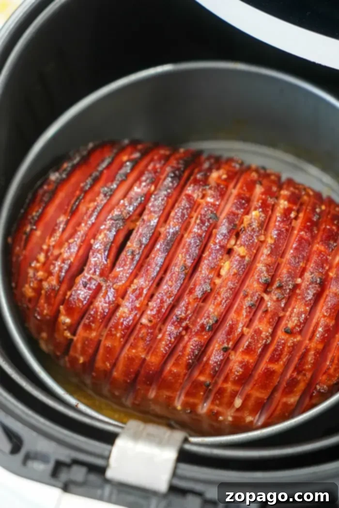 Crispy Air Fryer Ham 7 A honey-glazed air fryer ham with a scored surface is shown cooking. The exterior is caramelized to a golden brown with visible seasoning, resting perfectly in the round, black basket.