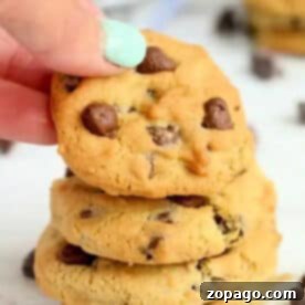 Effortless Cosori Air Fryer Creations 20 A hand with mint-green nail polish holds a chocolate chip cookie above a stack of air fryer cookies.