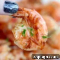 Effortless Cosori Air Fryer Creations 6 Close-up of a hand with glittery black nails holding a perfectly cooked shrimp, garnished with herbs, straight from the air fryer.