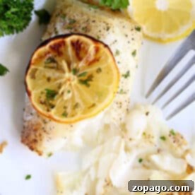Effortless Cosori Air Fryer Creations 8 Air fryer fish fillet baked to perfection, topped with a lemon slice and garnished with parsley, served on a white plate with a fork.