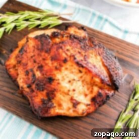Crispy Air-Fried Turkey Breast 7 air fryer boneless turkey breast with a crispy exterior rests on a wooden board, adorned with sprigs of rosemary. In the background, an air fryer turkey breast and a bowl of roasted potatoes sit charmingly on a striped cloth.
