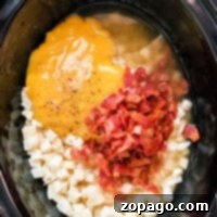 Ingredients in a crockpot: shredded cheese, frozen hashbrowns, chopped bacon, and seasoning simmer to create a savory potato soup.