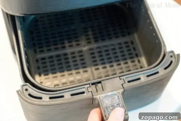 A hand pulling out an empty, mesh air fryer basket, ready for cooking chicken leg quarters.