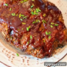 Versatile Ground Beef Recipes 11 Meatloaf cooked to perfection in a Ninja Foodi, topped with glaze and garnished with chopped chives on a white plate.