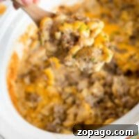 Versatile Ground Beef Recipes 14 A hand holds a wooden spoon above a crockpot filled with a cheesy hamburger casserole. This savory delight combines macaroni, ground beef, and melted cheese, all garnished with fresh herbs for that perfect finish.
