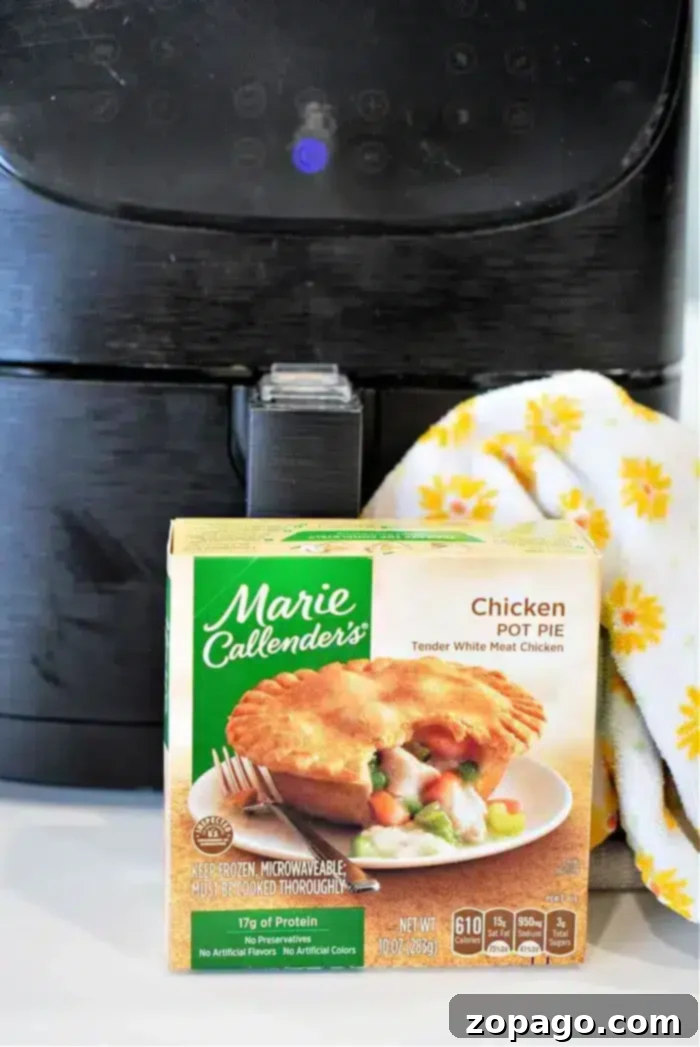Crispy Air Fryer Frozen Pot Pie 2 A Marie Callender's frozen pot pie box is placed in front of a black air fryer, ready for a crispy finish. A dish towel with yellow flowers is draped beside it, adding a touch of warmth to the scene.