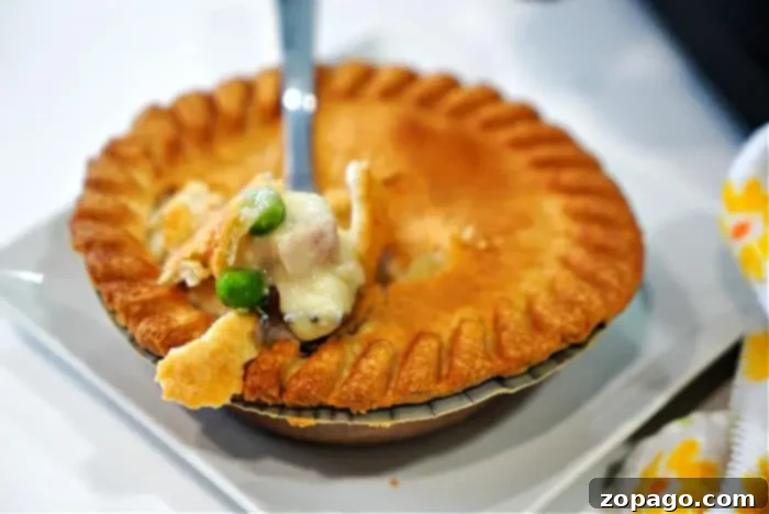 Crispy Air Fryer Frozen Pot Pie 10 A fork lifts a bite of creamy chicken pot pie with peas and carrots, fresh from a frozen pot pie cooked to perfection in an air fryer. The flaky, golden-brown crust has a beautiful fluted edge, and a patterned cloth is partially visible beside the white plate.
