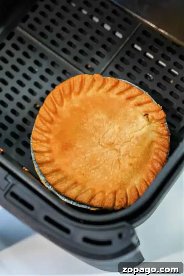 Crispy Air Fryer Frozen Pot Pie 6 A golden-brown frozen pot pie sits in an air fryer basket, its crust evenly baked with a decorative crimped edge. The air fryer features a perforated base for optimal air circulation, making it perfect for transforming frozen delights into crispy perfection.