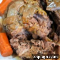 Slow-Cooked Dutch Oven Roast 9 Close-up of a tender, cooked beef pot roast with carrots and onions on a white plate, lovingly prepared in a dutch oven for rich flavor.