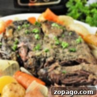 Tender pot roast with carrots, potatoes, and onions on a white plate in front of a slow cooker—perfect for making even a frozen roast in the slow cooker.
