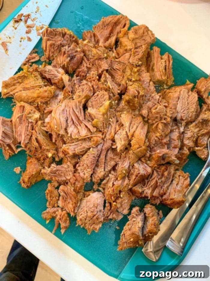 Slow Cooker Frozen Roast 11 Best chuck roast recipe showing a close up of tender, shredded beef with visible herbs.